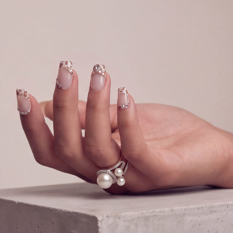 Side hand model wearing Sugar Kitten press-on nails with nude pink bases, leopard French tips, and sparkling rhinestone trim