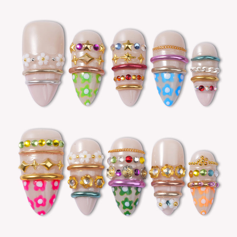 Sunset Gypsy handmade press-on nails arranged in a flat lay with nude bases, colorful charms, and gold accents on white