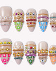 Sunset Gypsy handmade press-on nails arranged in a flat lay with nude bases, colorful charms, and gold accents on white