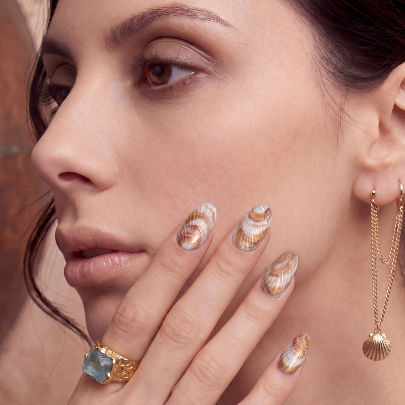 Close-up portrait of a woman wearing brown and white shell-pattern press-on nails with gold jewelry.
