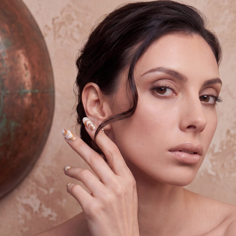 Portrait of a woman posing with brown and white shell-pattern press-on nails against a warm beige background.