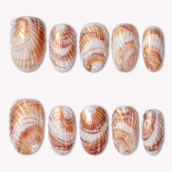 Sunset shell press on nails with warm orange and white shell-inspired swirls arranged in a flat lay on a white background