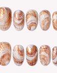 Sunset shell press on nails with warm orange and white shell-inspired swirls arranged in a flat lay on a white background