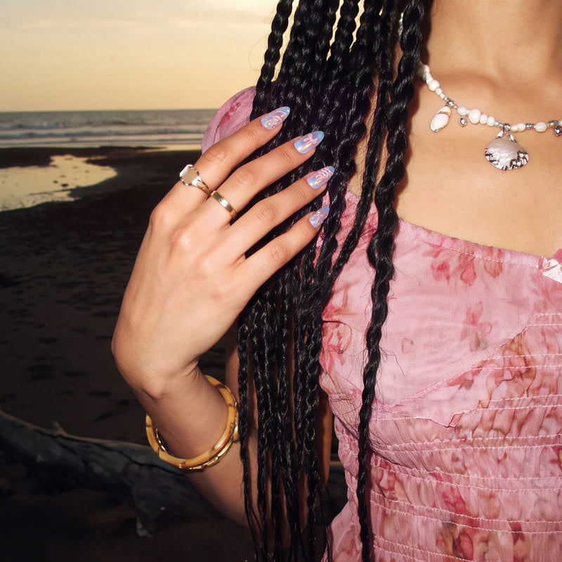 Beach lifestyle shot of Swan Ballet iridescent press-on nails worn with pearl jewelry and a pink dress