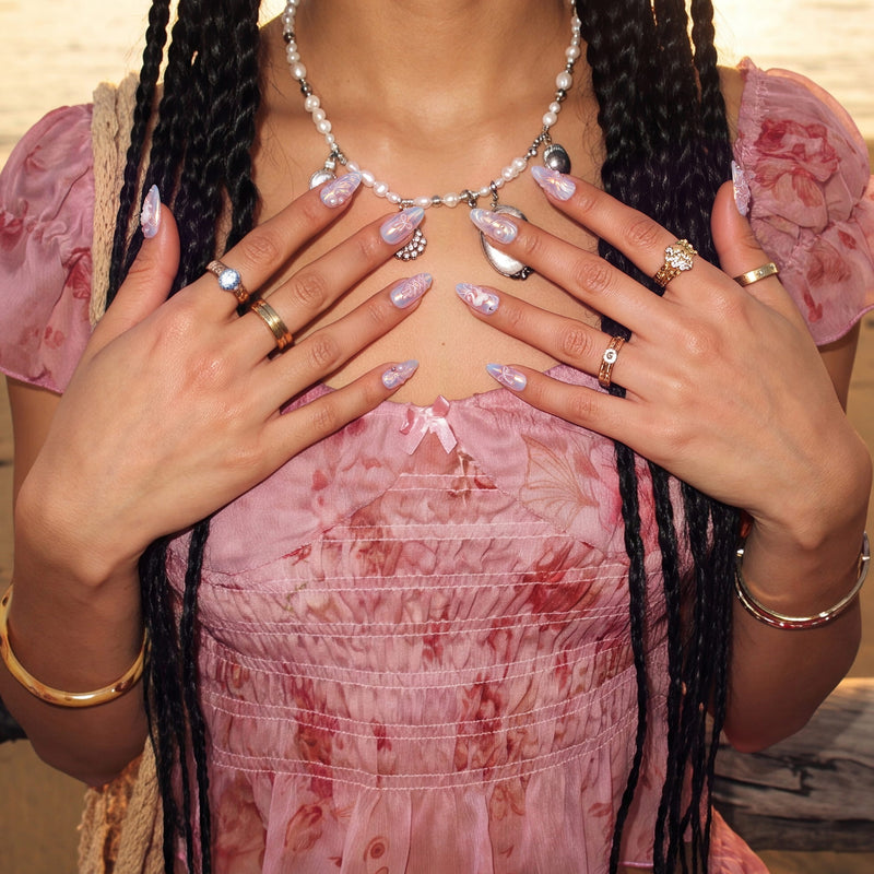 Model wearing Swan Ballet iridescent press-on nails with pearl jewelry and a pink floral dress