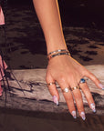 Hand close-up wearing Swan Ballet iridescent press-on nails with rings on a sunlit wooden rail