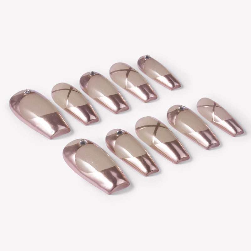 Angled flat lay of Swan Lake Dream press-on nails with rose gold metallic French tips, nude jelly bases, crisscross lines, and rhinestones