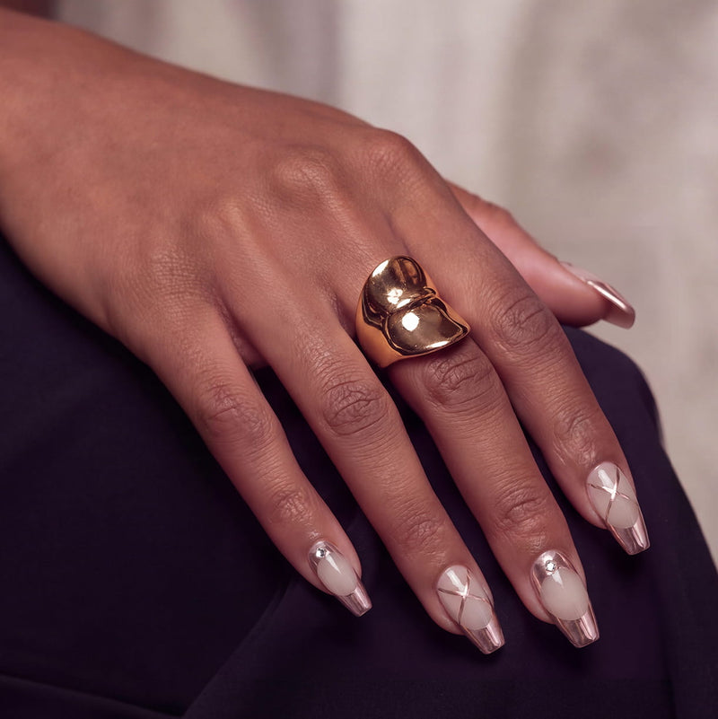 Lifestyle hand model wearing Swan Lake Dream press-on nails with rose gold metallic French tips, crisscross accents, and rhinestones
