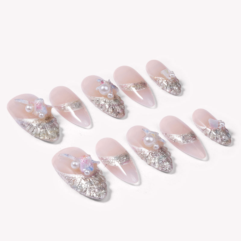 Flat lay of pale pink almond press-on nails with silver glitter waves and pearl floral accents on a white background.