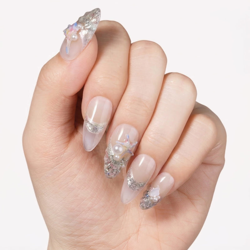 Hand close-up wearing silver shell-inspired press-on nails with pearl and starfish accents.
