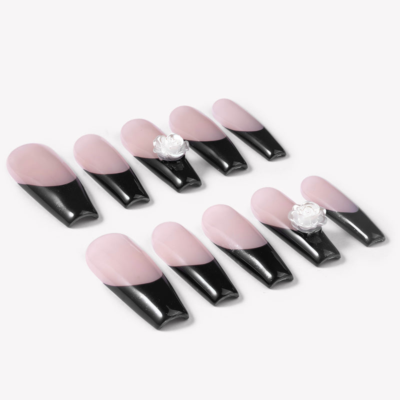 Angled flat lay of Timeless Serenity press-on nails with glossy nude bases, black French tips, subtle shimmer, and white flower accents