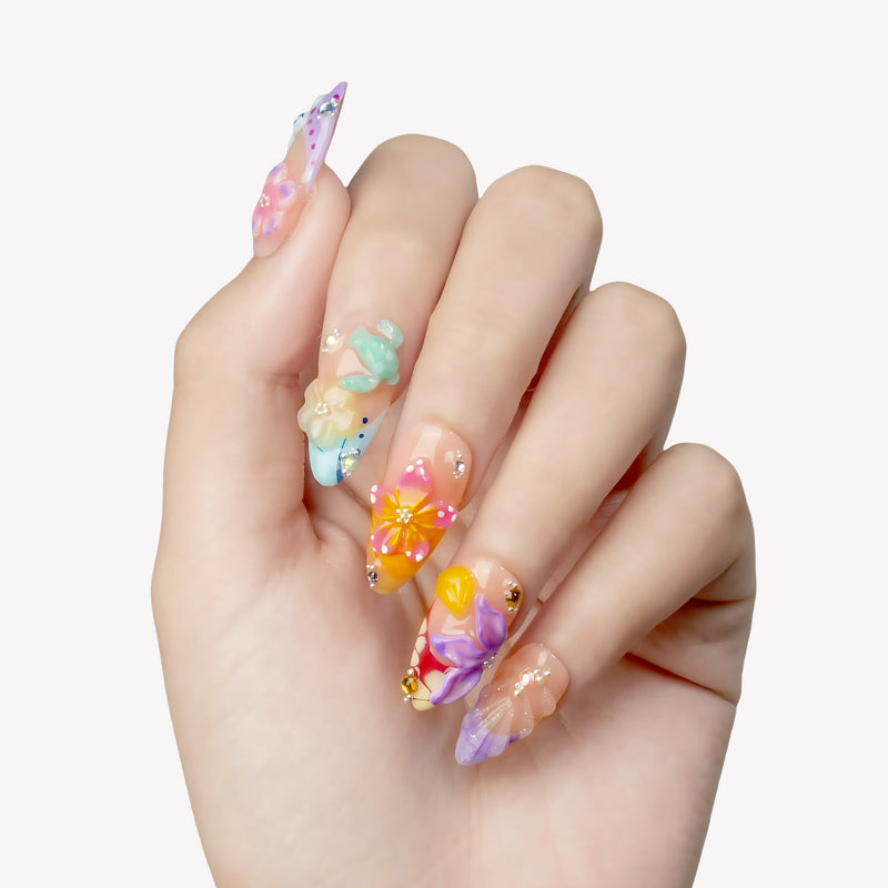 Hand close-up wearing Tropical Bloom long press-on nails with sculpted flowers, shells and crystal accents