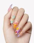 Hand close-up wearing Tropical Bloom long press-on nails with sculpted flowers, shells and crystal accents