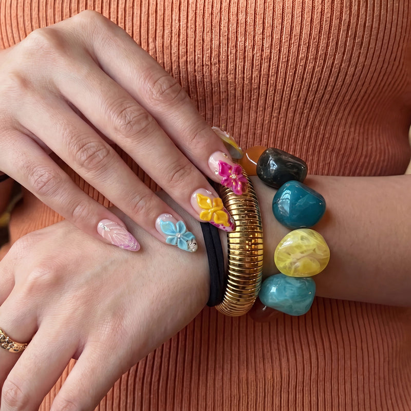 Close-up of Tropical Bloom raised floral press-on nails styled with colorful stone and gold bracelets