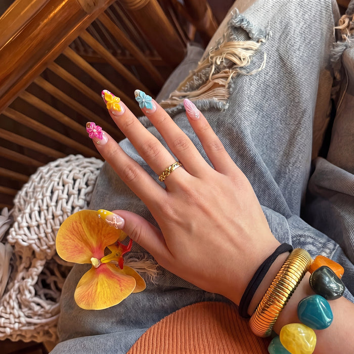 Hand model wearing Tropical Bloom colorful 3D floral press-on nails with denim and bold bracelets