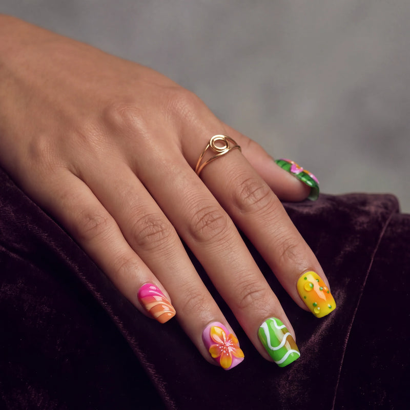 Close-up of a hand wearing Tropical Jelly Bloom press-on nails with floral art and bright green, pink, orange, and yellow accents