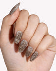 Hand model wearing beige and brown snakeprint press-on nails with long pointed shapes