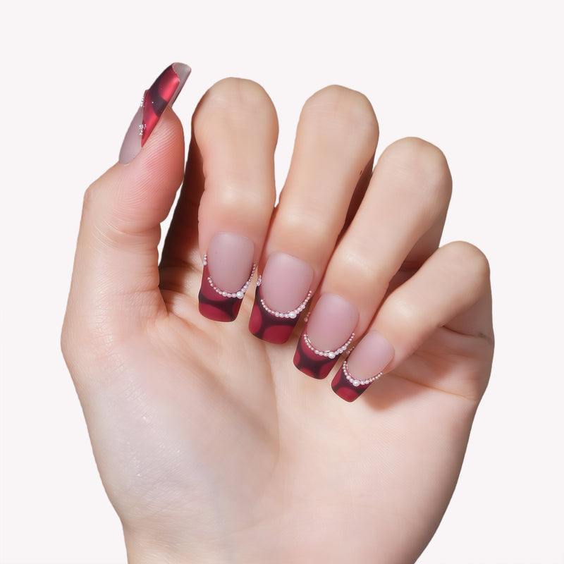 Close-up of a hand model wearing Vintage Ruby press-on nails in glossy red and black with pearl accents