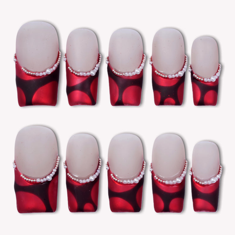 Flat lay of Vintage Ruby press-on nail swatches with glossy red and black bases and pearl accents