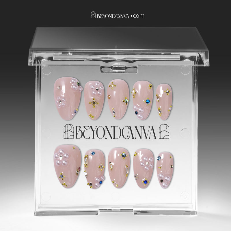 Press-on nails displayed inside a clear BeyondCanva case with nude pink stiletto nails, pearl clusters, and gold accents