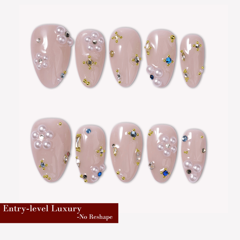 Nude pink almond press-on nails with pearl clusters, gold studs, and crystal accents arranged in a flat lay