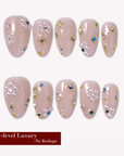 Nude pink almond press-on nails with pearl clusters, gold studs, and crystal accents arranged in a flat lay