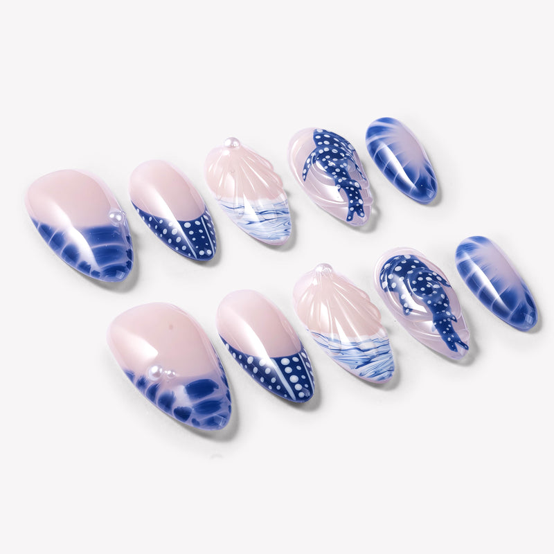 Flat lay of Whale Song press-on nails with blue ocean wave tips, whale tail design, white dot accents, seashell texture, pearl details, and glossy nude bases