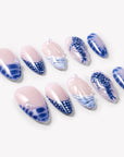 Flat lay of Whale Song press-on nails with blue ocean wave tips, whale tail design, white dot accents, seashell texture, pearl details, and glossy nude bases