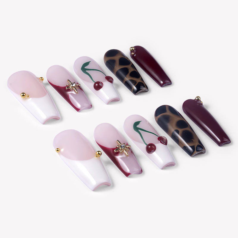 Angled flat lay of Wild Cherry press-on nails with burgundy cherry art, leopard print, sheer pink bases, and gold accents
