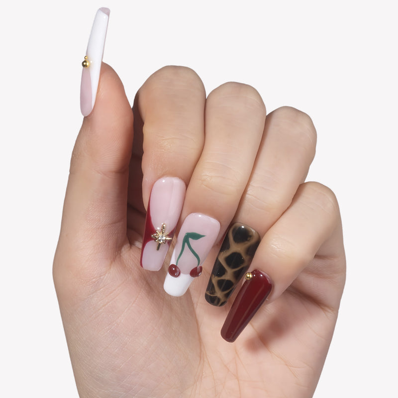 Hand model wearing Wild Cherry press-on nails with pink sheer bases, burgundy accents, cherry nail art, leopard print, and gold details