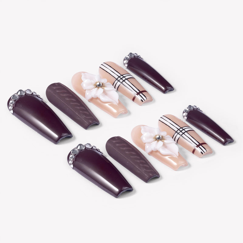 Angled flat lay of Winter Serenade press-on nails with deep purple rhinestone tips, textured accents, nude plaid lines, and white 3D flowers