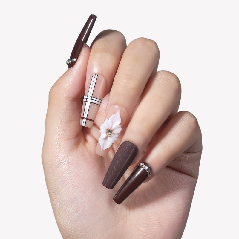 Close-up hand model wearing Winter Serenade press-on nails with deep purple rhinestone tips, nude plaid lines, and a white 3D flower