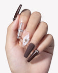 Close-up hand model wearing Winter Serenade press-on nails with deep purple rhinestone tips, nude plaid lines, and a white 3D flower