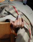 Lifestyle hand model wearing Winter Serenade press-on nails with purple tips, nude plaid accents, and a white 3D flower beside a plaid scarf